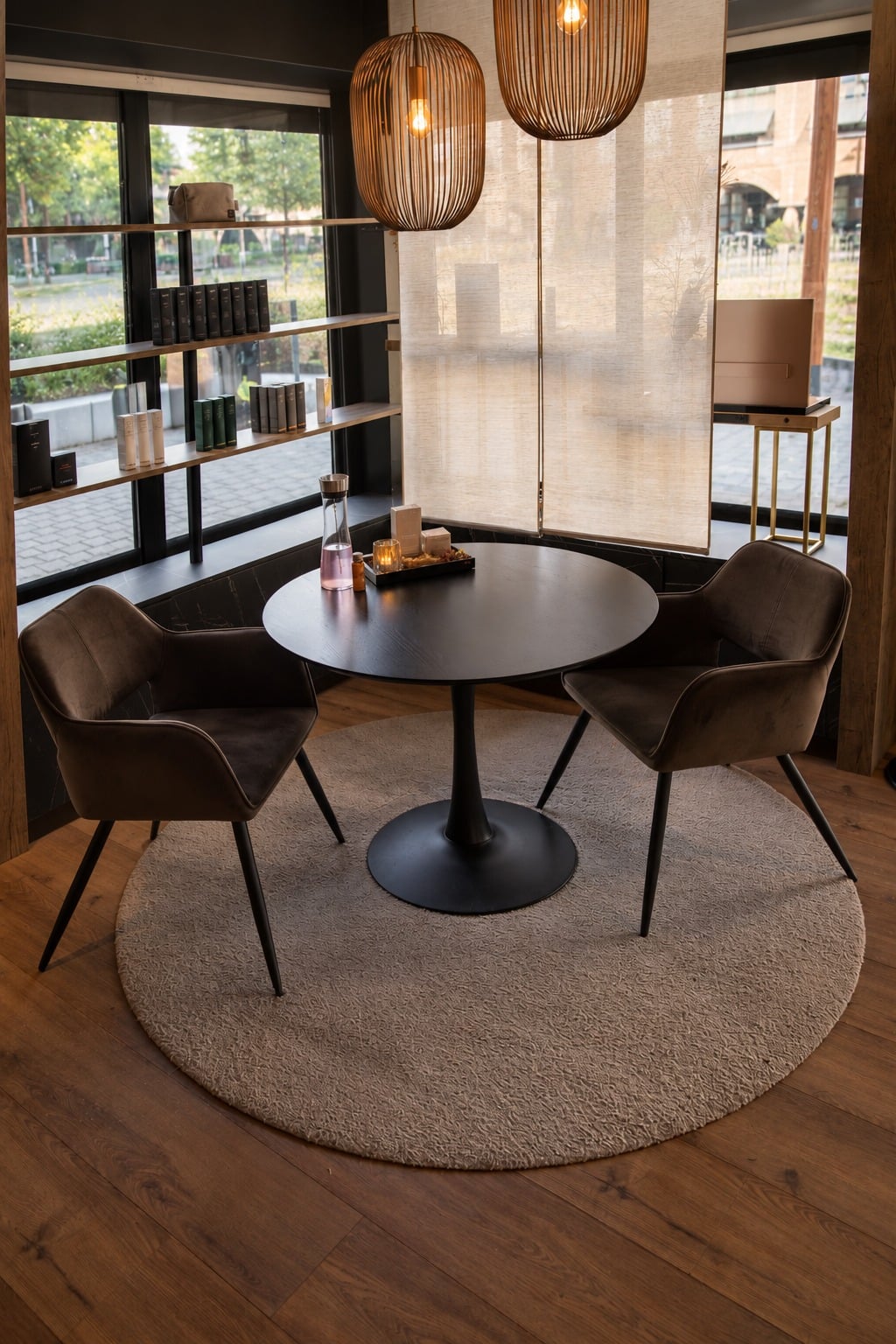 Zithoek bij SCENERY Beauty: ronde tafel met twee fluwelen stoelen onder rieten hanglampen, bij het raam