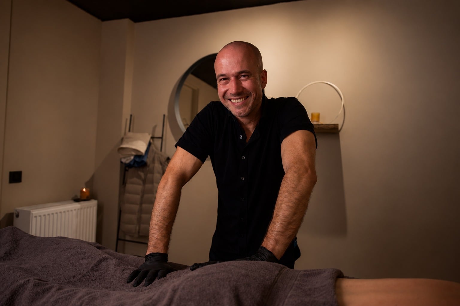Jeff lacht breed naast de behandeltafel, handen in zwarte handschoenen op de handdoek